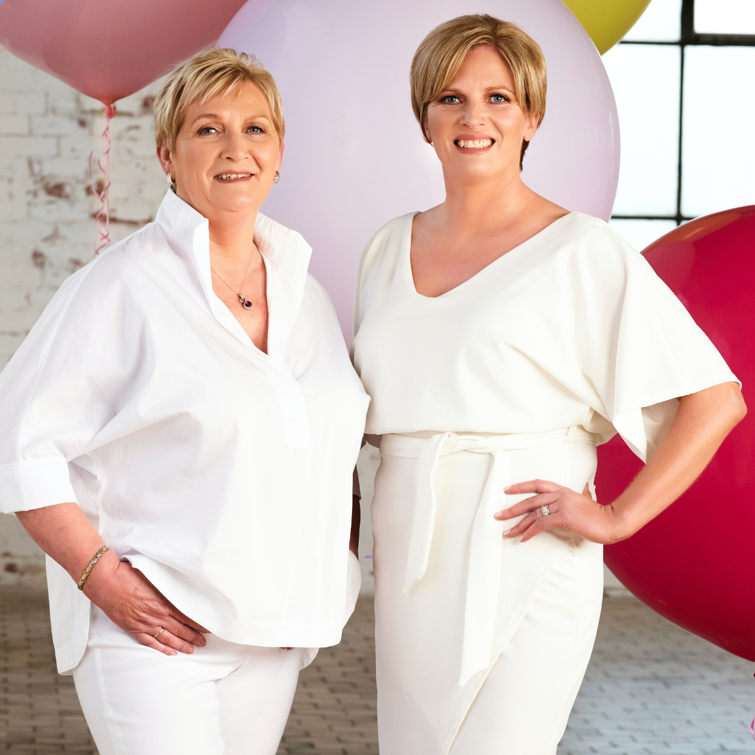 Image of He-Shi founders Shelley and Hilary in white outfits in front of large balloons of different colours