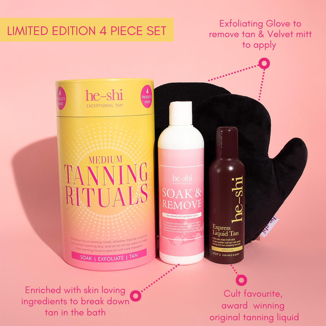 He-Shi Limited Edition 4-Piece Tanning Rituals Gift Set in medium, featuring a pink and yellow cylindrical box, Soak & Remove tan remover bubble bath, Express Liquid Tan, an exfoliating glove, and a velvet tanning mitt. Annotations highlight the exfoliating glove for tan removal, skin-loving ingredients to break down tan in the bath, and the cult-favourite Express Liquid Tan.