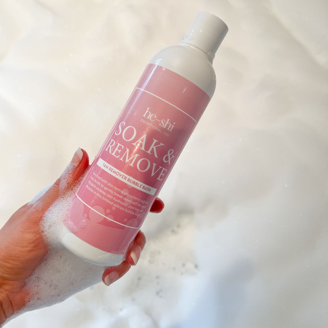 Image of hand holding a bottle of the He-Shi Soak & Remove Tan Removing Bubble Bath in the bath tub.