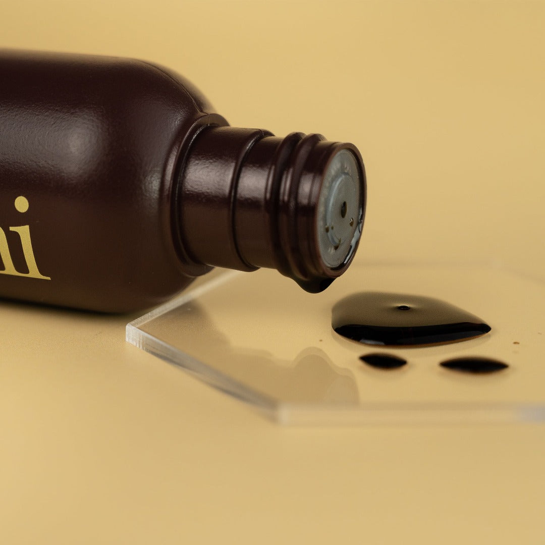 he-shi liquid tan bottle displayed on its side showing the texture of the product on a glass plinth 