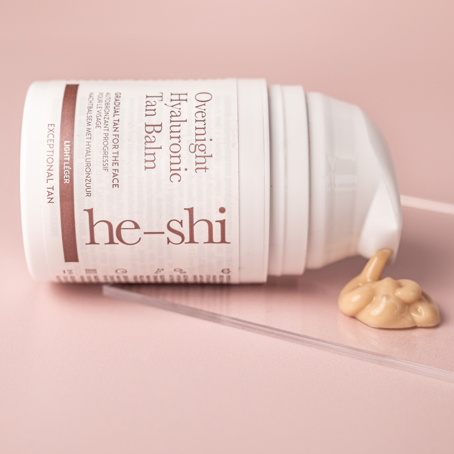 Image of He-Shi Overnight Hyaluronic Tan Balm on its side with product spilling out onto a glass plinth. 